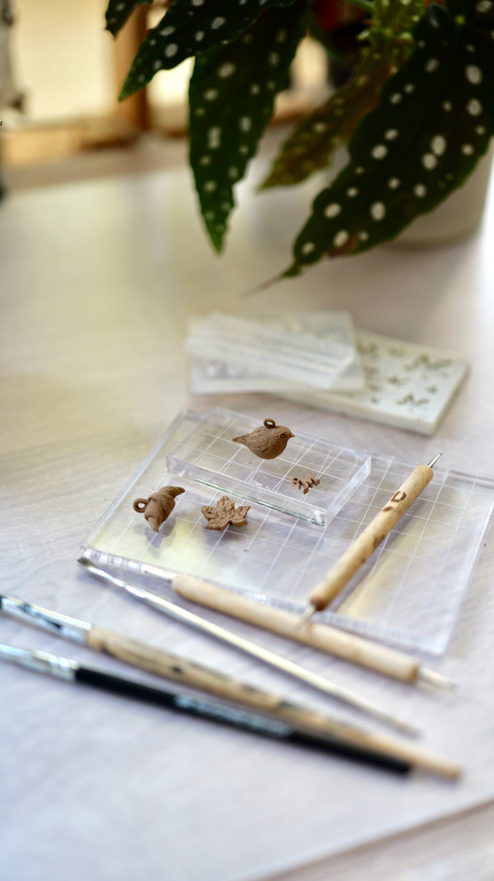 Detail na ukážku výrobkov z kurzu výroby šperkov z modelovacieho bronzu. Výrobky na podložke na bledom pozadí s modelovacími nástrojmi.