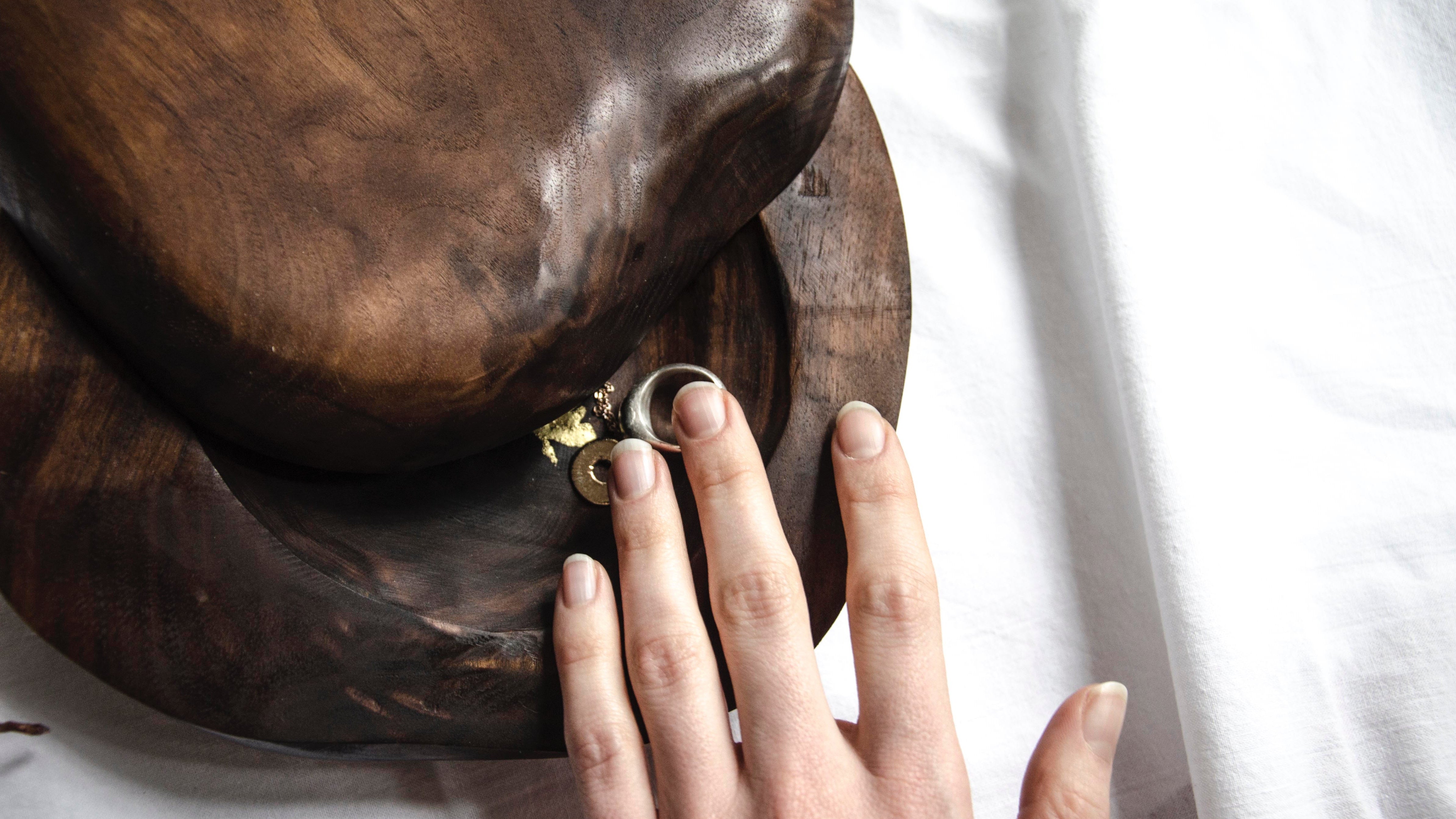 a detail on a hand reaching into an open wooden handcarved sculptural jewelry box.