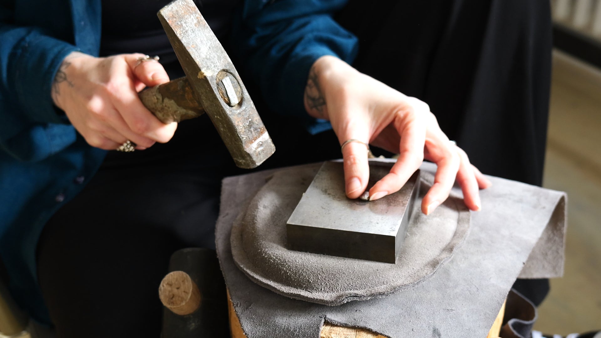 a shot of a silver smithing proces, female hands holding a hammer and preparing to work on a small piece of silver on an anvil