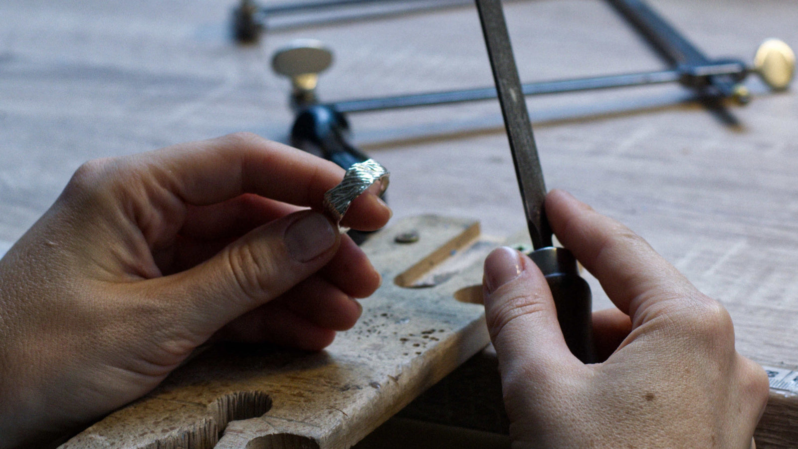 a detail on hands holding a ring and a jewelry making file, working on the ring at a jeweller's bench.