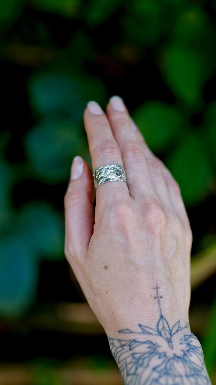 Výrazný široký prsteň zo striebra Ag 925/1000 s organickoou textúrou evokuje povrch vodnej hladiny, kde sa striebro prepletá do hladkých, vlnivých tvarov. Tento dizajn je doplnený o labradorit a mesačný kameň ktorého odlesky pripomínajú mystické hlbiny vody, akoby sa odrážali v pokojnej hladine.