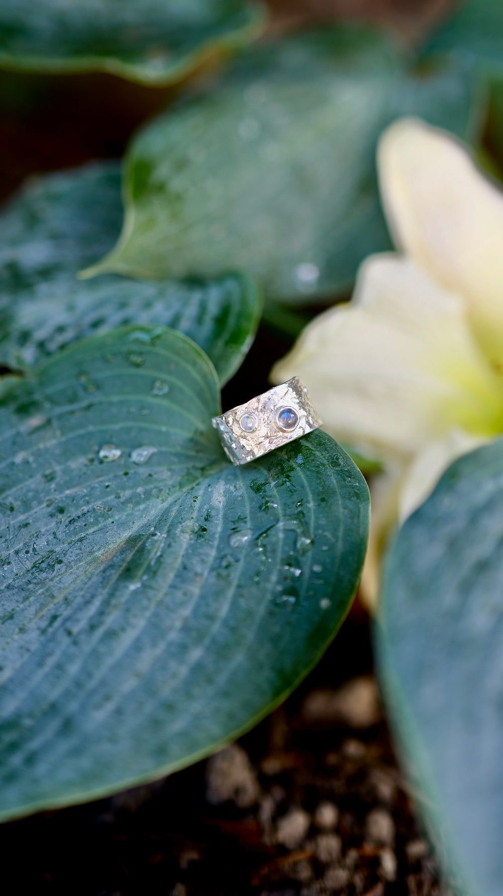 Výrazný široký prsteň zo striebra Ag 925/1000 s organickoou textúrou evokuje povrch vodnej hladiny, kde sa striebro prepletá do hladkých, vlnivých tvarov. Tento dizajn je doplnený o labradorit a mesačný kameň ktorého odlesky pripomínajú mystické hlbiny vody, akoby sa odrážali v pokojnej hladine.